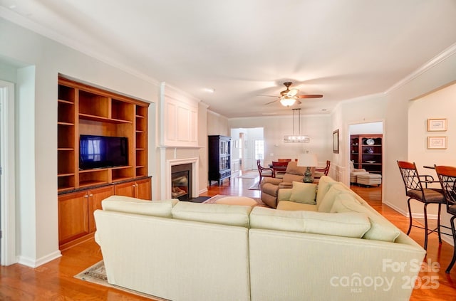 living area with light wood finished floors, baseboards, ceiling fan, ornamental molding, and a fireplace