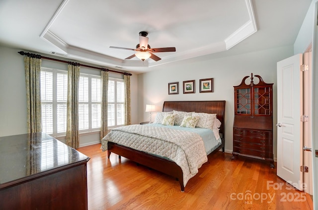 bedroom featuring baseboards, ornamental molding, wood finished floors, a raised ceiling, and a ceiling fan