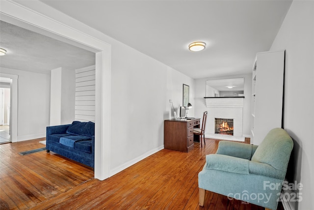 living area with a brick fireplace, baseboards, and hardwood / wood-style floors