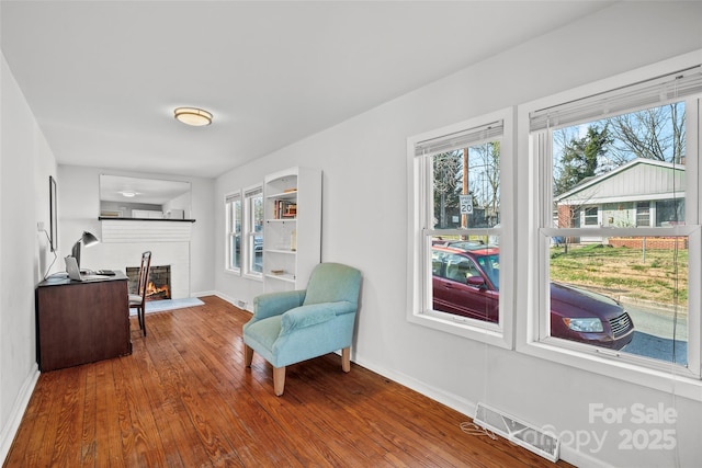 sitting room featuring visible vents, a healthy amount of sunlight, a lit fireplace, and hardwood / wood-style floors