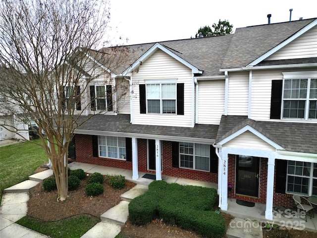 view of property featuring brick siding and roof with shingles