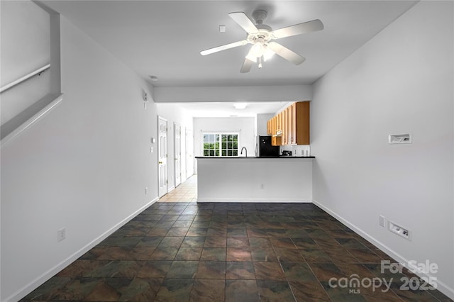 unfurnished living room with baseboards, stone finish flooring, ceiling fan, and a sink