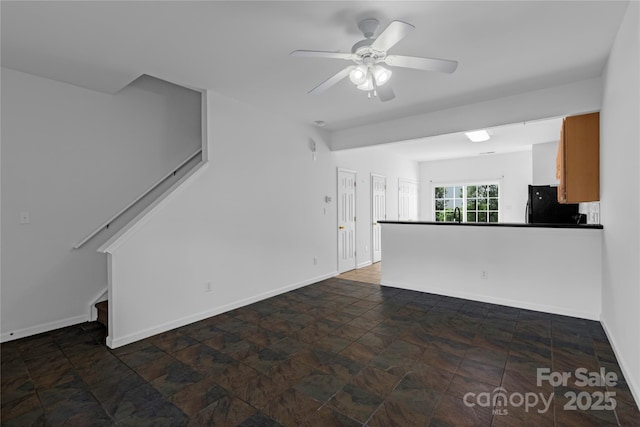 unfurnished living room featuring stairway, stone finish floor, a ceiling fan, and baseboards