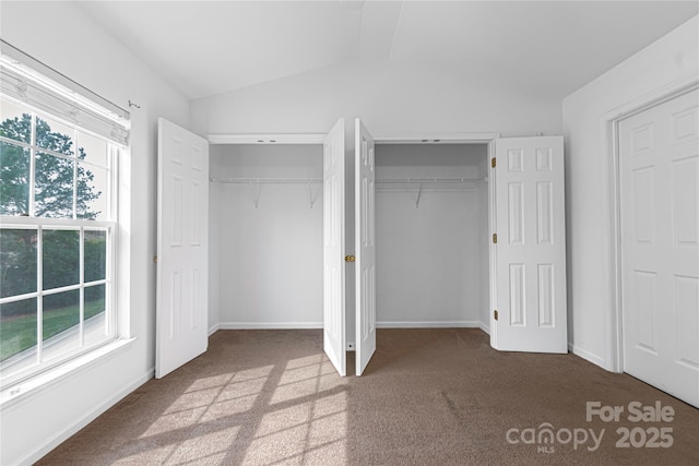 unfurnished bedroom with lofted ceiling, carpet, multiple closets, and baseboards