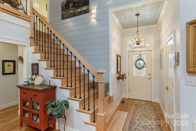 entrance foyer featuring baseboards, light wood-style flooring, ornamental molding, stairs, and a notable chandelier