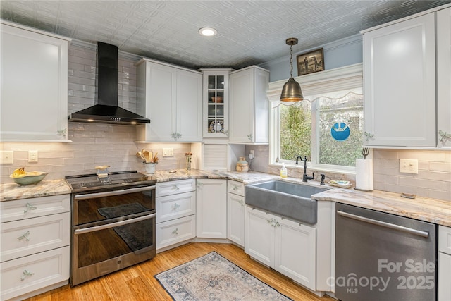 kitchen with an ornate ceiling, a sink, stainless steel appliances, white cabinetry, and wall chimney exhaust hood