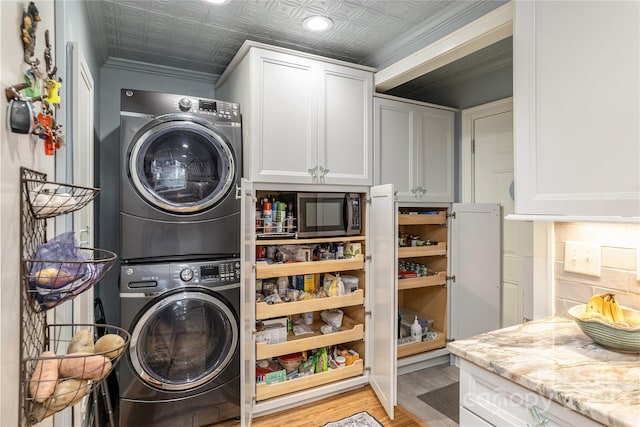 clothes washing area with light wood-type flooring, ornamental molding, stacked washer and dryer, cabinet space, and an ornate ceiling