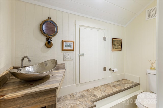 half bathroom with visible vents, toilet, crown molding, vanity, and vaulted ceiling