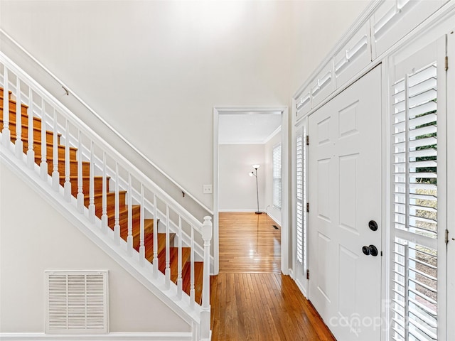 entryway featuring visible vents, crown molding, baseboards, stairs, and wood-type flooring