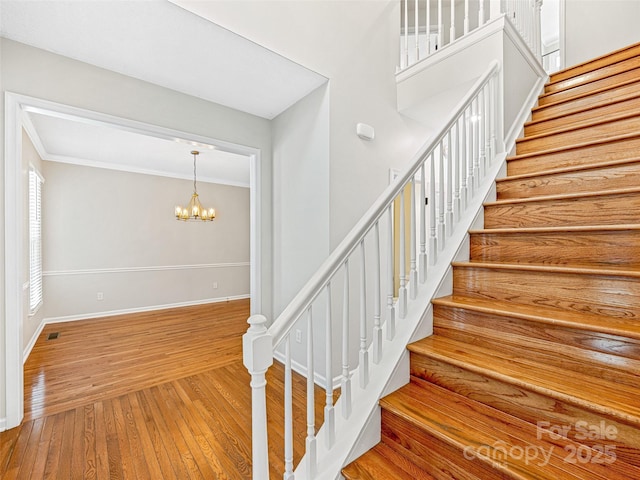 stairs with a chandelier, ornamental molding, baseboards, and hardwood / wood-style floors