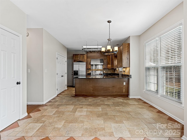 kitchen with dark countertops, wall chimney exhaust hood, stainless steel fridge, backsplash, and a chandelier