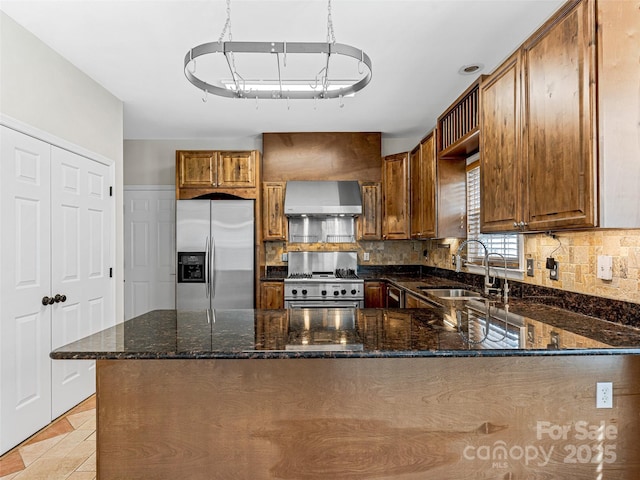 kitchen with a sink, stainless steel appliances, dark stone countertops, and wall chimney range hood