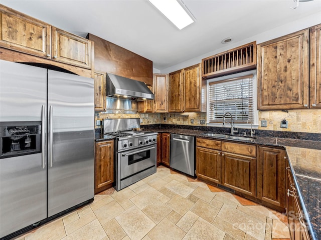 kitchen featuring dark stone countertops, a sink, stainless steel appliances, wall chimney exhaust hood, and backsplash