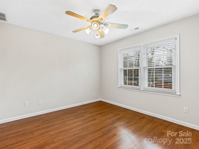 spare room with a textured ceiling, wood finished floors, visible vents, and baseboards