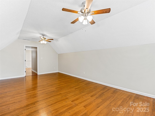 additional living space featuring baseboards, ceiling fan, light wood-type flooring, vaulted ceiling, and a textured ceiling