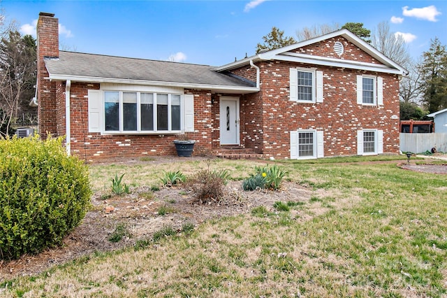 split level home featuring a front lawn, fence, brick siding, and a chimney