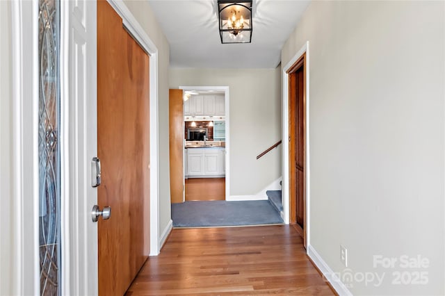 hall with stairway, baseboards, light wood-type flooring, and a chandelier