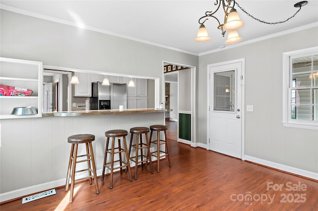 kitchen featuring stainless steel fridge with ice dispenser, a breakfast bar area, ornamental molding, dark wood-style floors, and a notable chandelier