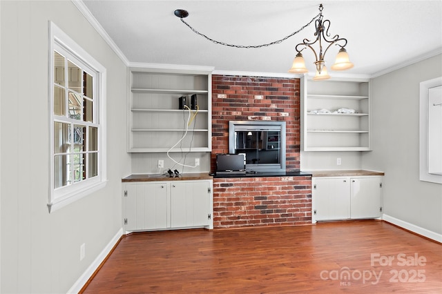 interior space with built in shelves, crown molding, baseboards, dark wood finished floors, and a notable chandelier