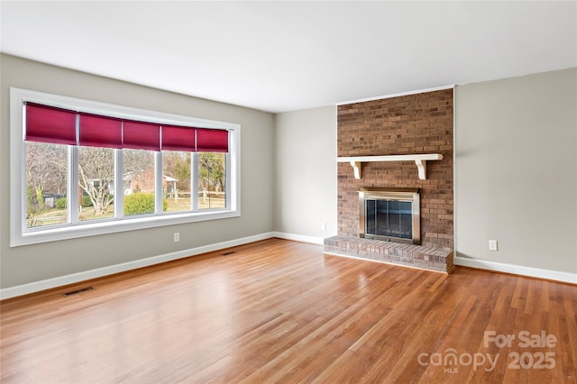 unfurnished living room with a brick fireplace, wood finished floors, visible vents, and baseboards