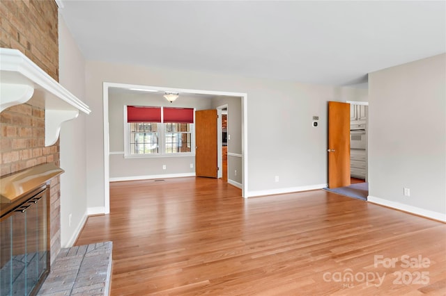 unfurnished living room featuring light wood-type flooring, baseboards, and a brick fireplace