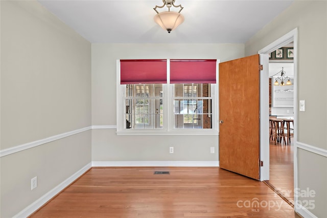 unfurnished room featuring visible vents, a notable chandelier, wood finished floors, and baseboards