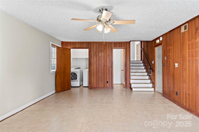 unfurnished living room featuring wooden walls, stairs, a textured ceiling, a ceiling fan, and separate washer and dryer