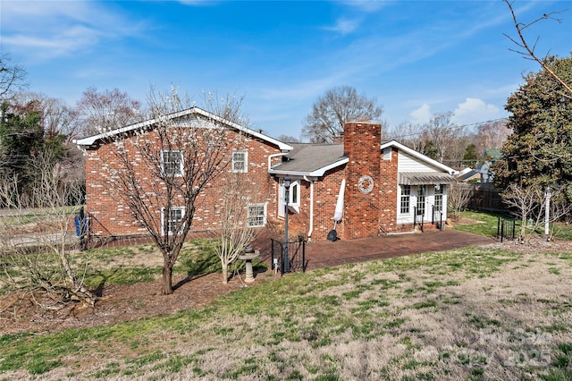 rear view of house featuring fence, a yard, a chimney, a patio area, and brick siding