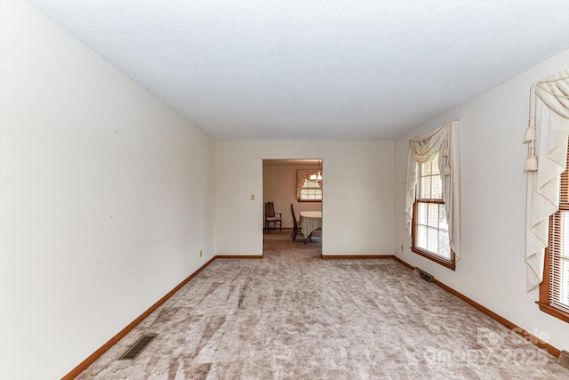 carpeted empty room with visible vents, a textured ceiling, and baseboards