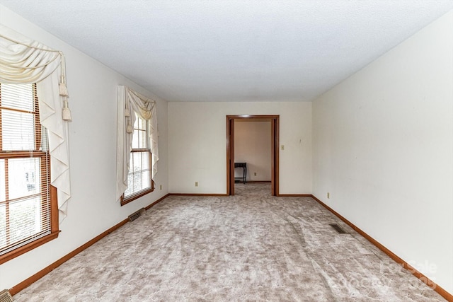 carpeted spare room with visible vents, baseboards, and a textured ceiling