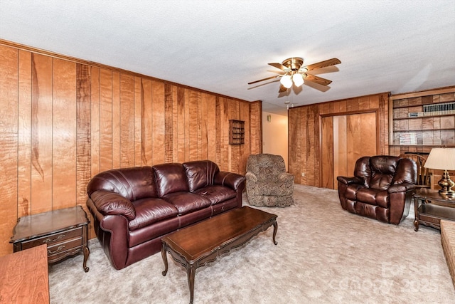 carpeted living room featuring wooden walls, a ceiling fan, and a textured ceiling