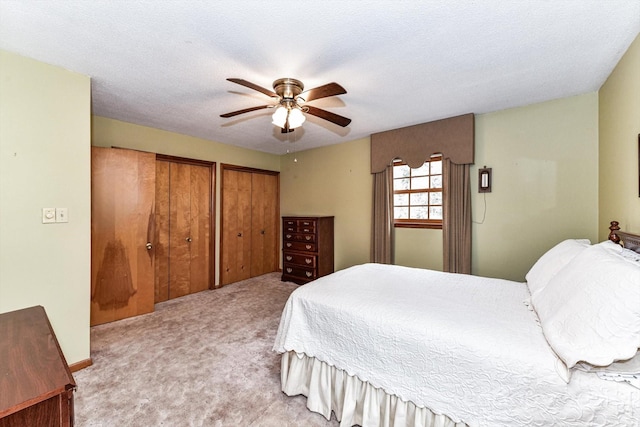 bedroom featuring a textured ceiling, ceiling fan, two closets, and light carpet