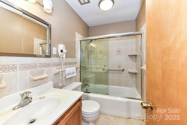 bathroom with tile patterned floors, toilet, combined bath / shower with glass door, tile walls, and vanity