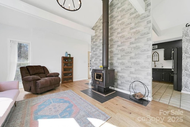 living room featuring beamed ceiling, high vaulted ceiling, light tile patterned floors, baseboards, and a wood stove