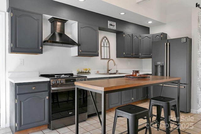 kitchen featuring stainless steel range with gas stovetop, recessed lighting, a sink, wall chimney exhaust hood, and refrigerator with ice dispenser