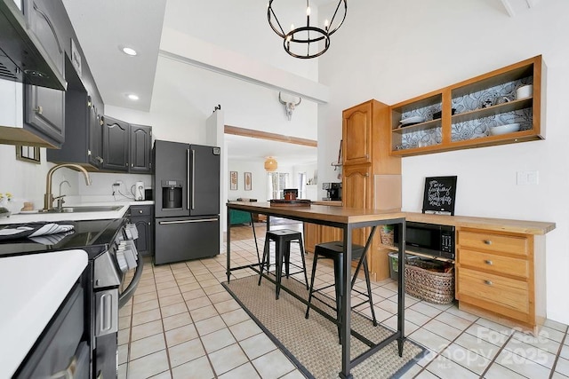 kitchen with black appliances, a sink, under cabinet range hood, light tile patterned flooring, and light countertops