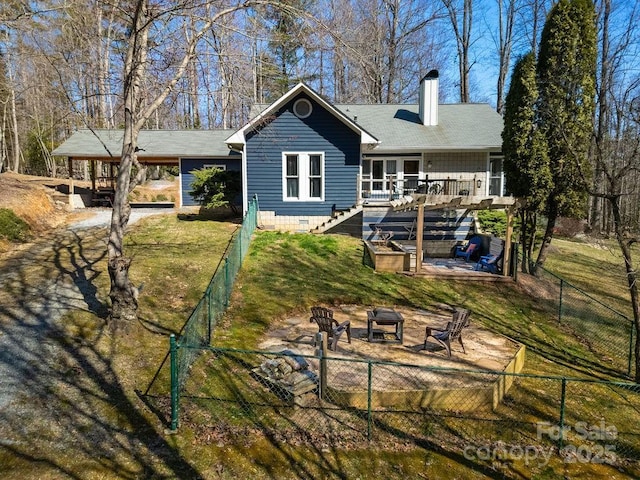 rear view of house with fence, an outdoor fire pit, a chimney, a deck, and a lawn