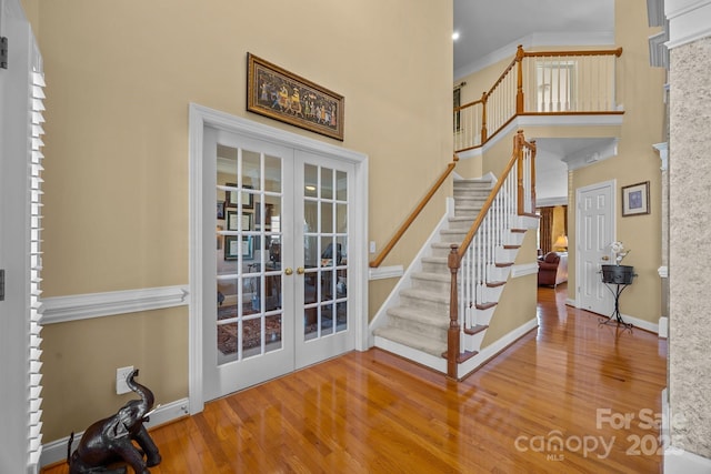 entrance foyer with french doors, stairs, a high ceiling, and wood finished floors