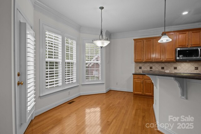 561 Keystone Ct NW, Concord, NC 28027 - kitchen with stainless steel microwave, decorative backsplash, light wood finished floors, hanging light fixtures, and crown molding