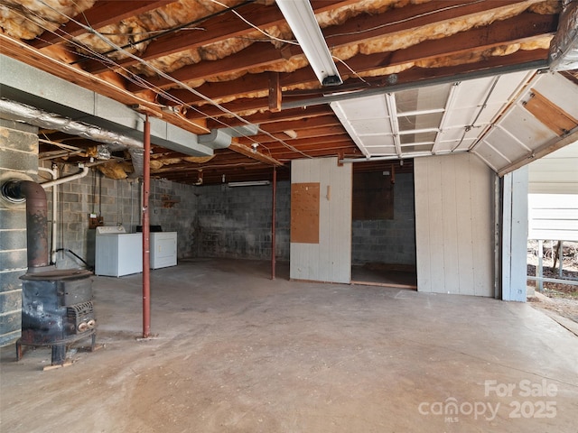 unfinished below grade area featuring a wood stove, concrete block wall, and separate washer and dryer