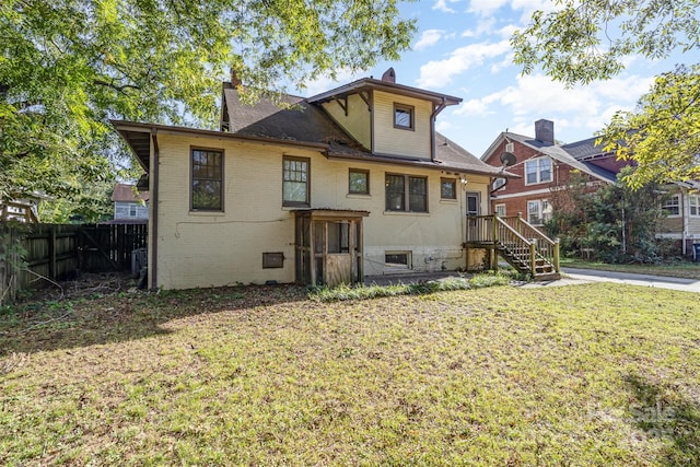 rear view of property featuring brick siding, fence, a lawn, and a chimney