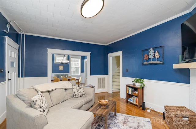 living room with a wainscoted wall, ornamental molding, stairs, and a chandelier