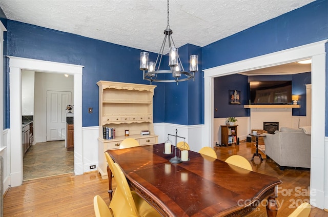 dining area with a notable chandelier, a textured ceiling, wood finished floors, wainscoting, and a fireplace