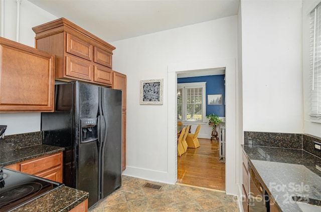 kitchen featuring dark stone countertops, visible vents, black fridge with ice dispenser, and brown cabinetry