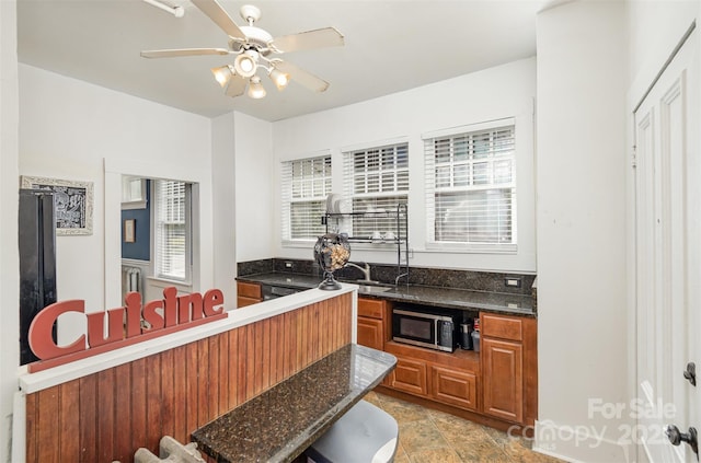 kitchen featuring stainless steel microwave, dark stone countertops, brown cabinets, and ceiling fan