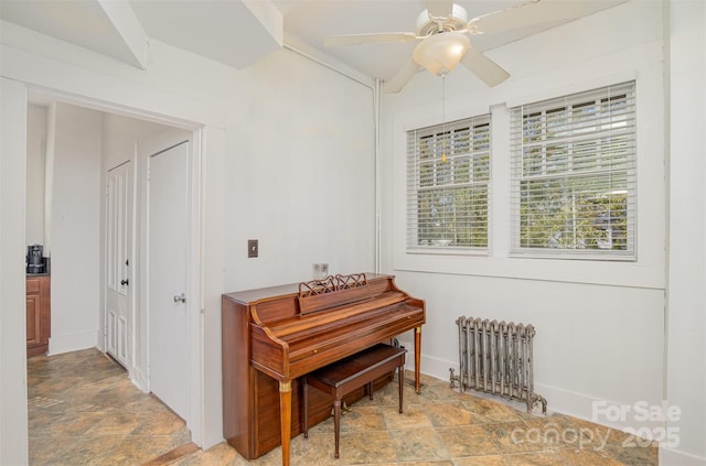 living area with baseboards, a ceiling fan, radiator heating unit, and stone finish floor