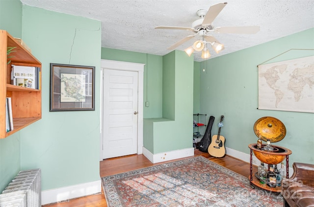 sitting room featuring a ceiling fan, a textured ceiling, wood finished floors, radiator, and baseboards