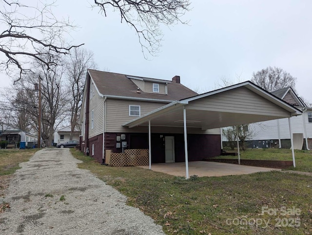 back of house with a yard, driveway, an attached carport, and a chimney