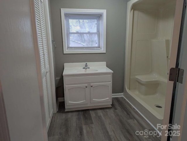 bathroom featuring vanity, a shower, baseboards, and wood finished floors