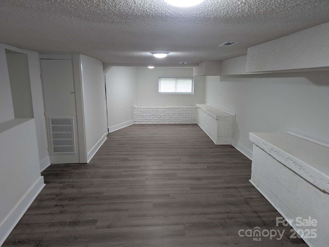 basement with visible vents, baseboards, a textured ceiling, and dark wood finished floors